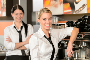 Zwei junge Frauen stehen zufrieden vor einer Kaffeemaschine