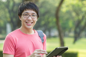 Ein junger Mann mit asiatischer Herkunft schaut lächelnd von seinem Tablet auf